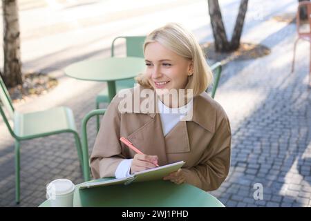 Bild einer jungen lächelnden Frau, die im Café sitzt, Skizzen macht, Kunst auf der Straße zeichnet, Zeit im Café verbringt und c Stockfoto