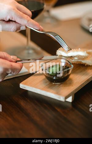Nahaufnahme der Hände eines Mannes, der Messer und Gabel hält und ein Stück paniertes Essen auf einem Holztisch schneidet. Stockfoto