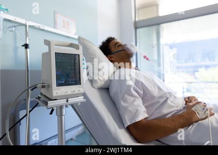 Birassischer männlicher Patient mit Sauerstoffmaske im Bett im sonnigen Krankenhauszimmer Stockfoto