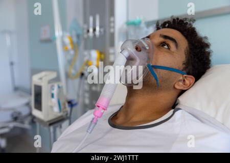 Birassischer männlicher Patient mit Sauerstoffmaske im Bett im sonnigen Krankenhauszimmer Stockfoto