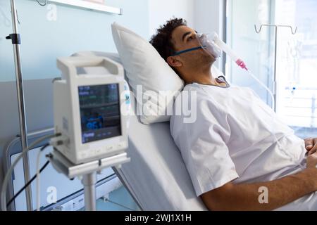 Birassischer männlicher Patient mit Sauerstoffmaske im Bett im sonnigen Krankenhauszimmer Stockfoto
