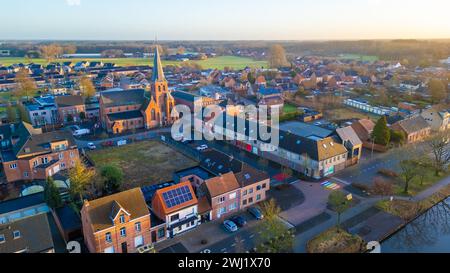 Diese Luftaufnahme fängt die malerische Stadt Rijkevorsel während des sanften Lichtes der Abenddämmerung ein. Die Sint Jozef Church mit ihrem hoch aufragenden Turm steht in den umliegenden Wohngebäuden. Das Bild bietet einen Einblick in die Stadtplanung und zeigt die Kirche als zentrales Wahrzeichen. Das warme Leuchten der untergehenden Sonne taucht die Stadt in ein gemütliches Licht und hebt die Dächer und die Architektur der Kirche vor dem Hintergrund der fernen Landschaft hervor. Luftaufnahme der Sint Jozef Church, Rijkevorsel in der Abenddämmerung. Hochwertige Fotos Stockfoto