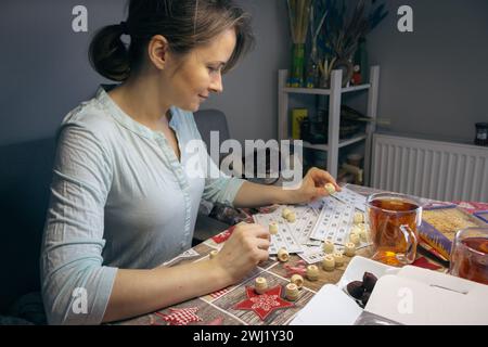 Mädchen spielt im Lotto mit dem Fass in der Hand. Nostalgie Lifestyle. Lächelnde Frau, die Bingo spielt. Freizeitaktivität. Retro-Tischspiele. Glückskonzept. Stockfoto