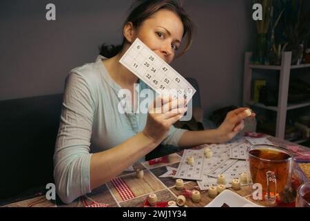 Mädchen spielt im Lotto. Nostalgie Lifestyle. Frau spielt Bingo und hält Karte. WIN-Konzept. Freizeitaktivität. Retro-Tischspiele. Glückskonzept. Stockfoto