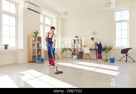 Junge männliche Putzfrauen im Overall, die Zimmerreinigungsaufgaben erledigen Stockfoto