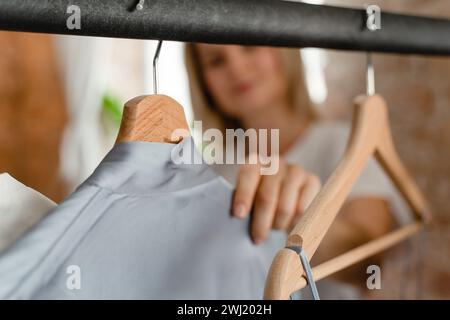 Die Frau durchsucht ihre verschiedenen Outfits, die an der Kleiderstange in ihrem Kleiderschrank hängen Stockfoto