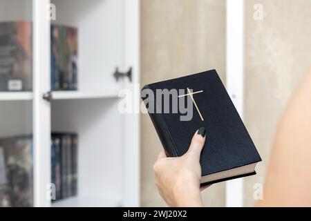 Der Mann nimmt eine Bibel aus einem Bücherregal. Ein Mann, der die Bibel im Bücherregal verstaut. Frau mit Bibel Stockfoto