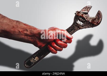 Männliche Hand mit verstellbarem Schraubenschlüssel in Blutflecken, die Schatten auf weißem Hintergrund werfen Stockfoto