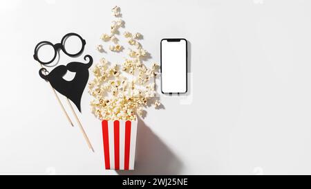 Köstliches Popcorn, Partyrequisiten und Smartphone mit leerem Bildschirm für Ihr Design Stockfoto