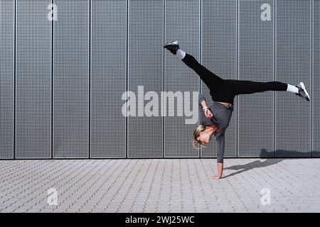 Sportlerin in weiblicher Sportbekleidung, die auf der Straße Radbewegungen macht Stockfoto