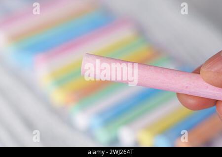 Pastellrosa Kreide in der Hand eines Kunstlehrers Nahaufnahme auf einem mehrfarbigen Buntstiftkollektion Hintergrund Stockfoto