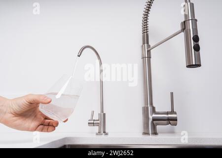 Frau bekommt gefiltertes Wasser aus rostfreiem Wasserhahn in ein Glas Stockfoto