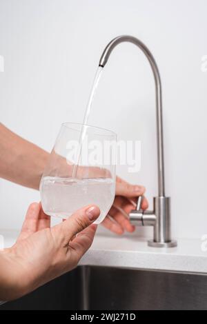 Frau bekommt gefiltertes Wasser aus rostfreiem Wasserhahn in ein Glas Stockfoto