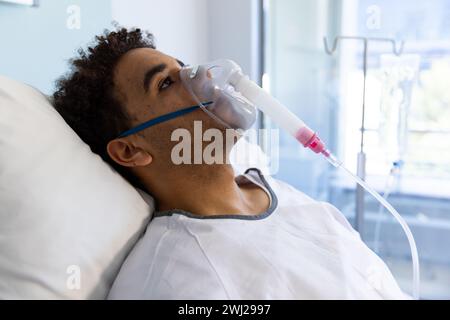 Birassischer männlicher Patient mit Sauerstoffmaske im Bett im sonnigen Krankenhauszimmer Stockfoto