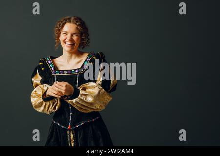 Porträt einer jungen lachenden Frau in einem mittelalterlichen Kleid auf dunklem Hintergrund. Stockfoto