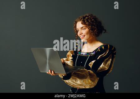 Porträt einer jungen Aristokratin in einem mittelalterlichen Kleid, die am Laptop arbeitet. Stockfoto