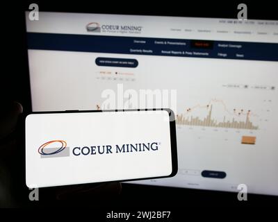 Person, die ein Mobiltelefon mit dem Logo des amerikanischen Edelmetallunternehmens Coeur Mining Inc. Vor der Business-Webseite hält. Schwerpunkt auf dem Display des Telefons. Stockfoto