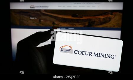 Person, die ein Smartphone mit dem Logo des US-Edelmetallunternehmens Coeur Mining Inc. Vor der Website hält. Schwerpunkt auf dem Display des Telefons. Stockfoto