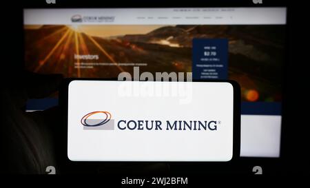 Person, die ein Mobiltelefon mit dem Logo des US-amerikanischen Edelmetallunternehmens Coeur Mining Inc. Vor der Webseite des Unternehmens hält. Schwerpunkt auf dem Display des Telefons. Stockfoto
