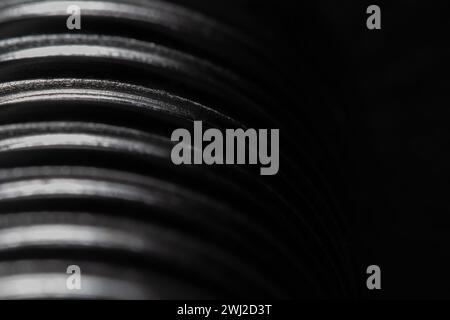 Nahaufnahme des Gewindes einer Metallschraube auf schwarzem Hintergrund, strukturiertes Metall, abstraktes Makro Stockfoto