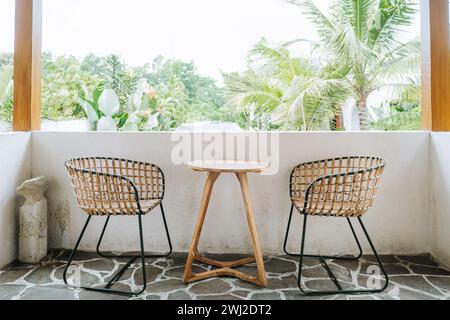 Zwei gewebte Stühle und ein Holztisch auf dem Balkon. Tropisches Café-Konzept. Stockfoto