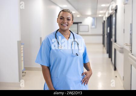 Porträt einer glücklichen birassischen Ärztin mit Peelings und Stethoskop im Spitalflur Stockfoto