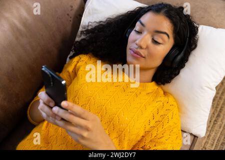 Birassische Frau mit Kopfhörern, die zu Hause auf dem Sofa liegt Stockfoto