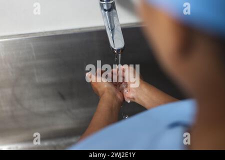 Mittelteil einer birassischen Ärztin mit Peelings, die im Operationssaal Hände waschen Stockfoto