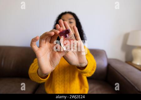 Birassische Frau in gelbem Pullover, die Videoanrufe macht und Kosmetikflasche zu Hause zeigt Stockfoto