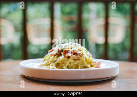 Ein Teller Spaghetti Carbonara mit Pilzen und Fleisch garniert mit Kräutern und geriebenem Käse darauf. Auf einer Holzfläche platziert. Stockfoto