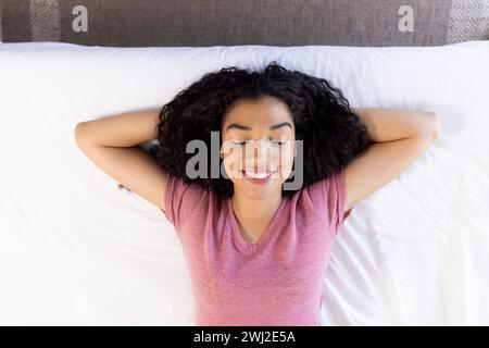 Blick auf die glückliche birassische Frau, die im Bett in sonnigem Haus liegt Stockfoto