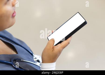 Birassische Ärztin mit Peelings mit Smartphone mit Kopierraum im Krankenhauskorridor Stockfoto