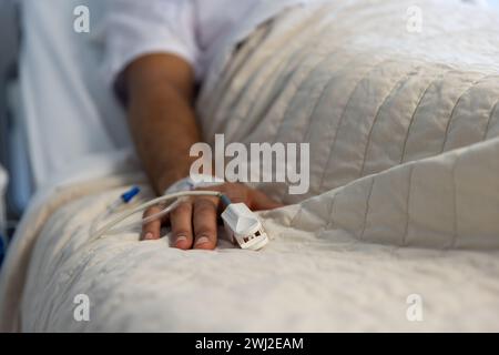 Die Hand eines männlichen Birazialisten mit IV-Tropf im Bett im sonnigen Krankenhauszimmer liegend Stockfoto