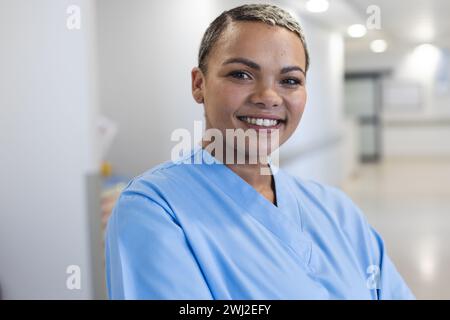 Porträt einer glücklichen birassischen Ärztin mit kurzen Haaren, die Peelings im Spitalflur trägt Stockfoto