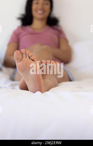 Die Beine einer glücklichen, birassischen Frau, die im sonnigen Haus auf dem Bett liegt Stockfoto