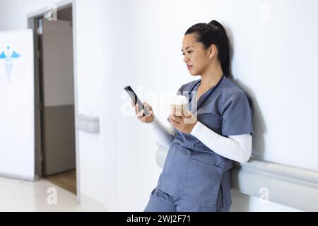 Zweirassige Ärztin mit Handschuhen mit Smartphone, mit Kaffee zum Mitnehmen, Kopierraum Stockfoto