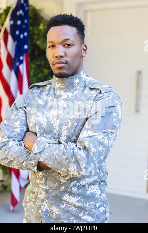 Männlicher afroamerikanischer Soldat, der mit Armen vor dem Haus steht, mit us-Flagge, Kopierraum Stockfoto