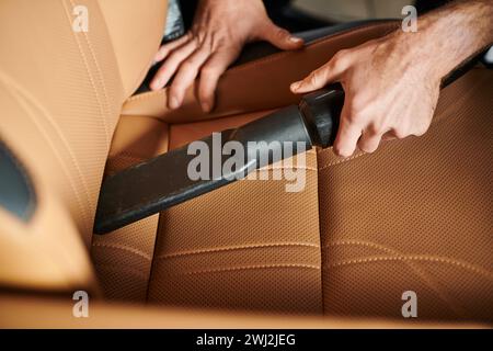 Zugeschnittene Ansicht eines professionellen Spezialisten, der Handstaubsauger im Auto in der Garage verwendet Stockfoto