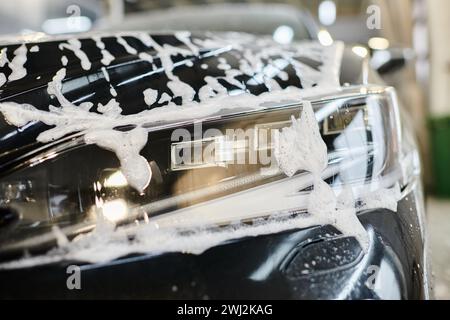Objektfoto des Scheinwerfers eines schwarzen modernen Autos, bedeckt mit Seife während des Waschens in der Garage Stockfoto