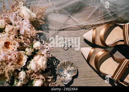 Hochzeitsringe, Brautschuhe und ein Blumenstrauß liegen auf einem Holztisch. Draufsicht Stockfoto