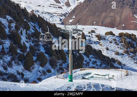 Skifahrer und Snowboarder fahren mit einem Skilift hinauf, der zum Gipfel der Berghänge führt. Seilbahnstange, Bau. Winterurlaub Aktivität, Lifestyle. Stockfoto