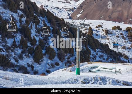 Die Leute steigen mit dem Skilift hoch, der zum Gipfel des Berghanges führt. Seilbahnstange, Bau. Winterurlaub Aktivität, Skifahrer, Snowboarder, lifestyl Stockfoto