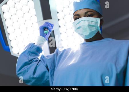 Porträt einer birassischen Chirurgin mit Operationsmantel und Gesichtsmaske im Operationssaal Stockfoto
