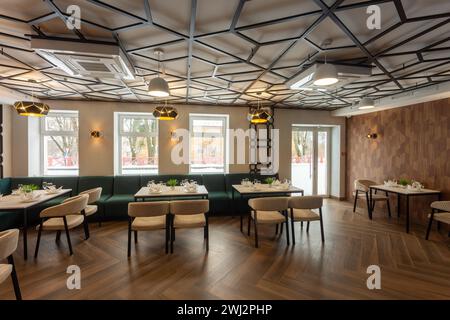 Modernes Interieur eines städtischen Restaurants oder Cafés mit Restaurants. Sanfte grüne Sofas und beige Stühle an Tischen, serviert mit Gläsern, Tellern und Servietten Stockfoto