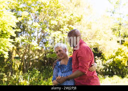 Glückliches, vielseitiges Seniorenpaar, das im sonnigen Garten tanzt Stockfoto