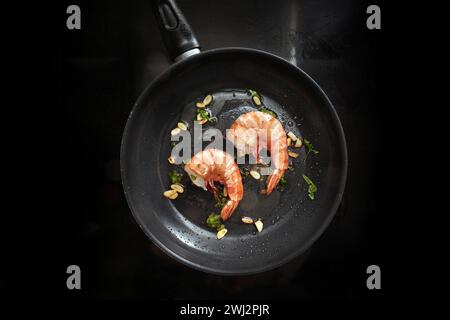 Frittieren Sie Jumbo-Tigergarnelen in Olivenöl mit Knoblauch und Kräutern in einer Pfanne auf einem schwarzen Herd, und kochen Sie ein Gourmet-Meeresfrüchte-Menü mit Stockfoto