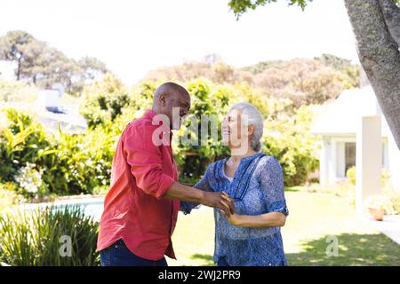 Glückliches, vielseitiges Seniorenpaar, das im sonnigen Garten tanzt Stockfoto