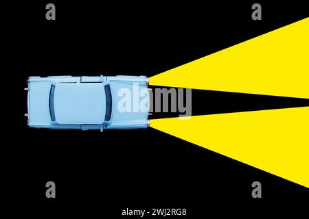 Hellblaues Retro-Autospielzeugmodell und Xenon-Lampe Scheinwerferkonzept auf schwarzem Hintergrund. Mietwagen, Stockfoto