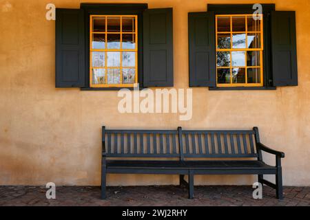 Außenwand eines Gebäudes mit zwei Fenstern, Fensterläden passend zur Bank, die darunter sitzt. Stockfoto