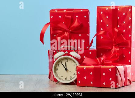 Wecker und Stapel roter Geschenkboxen auf blauem Hintergrund Stockfoto